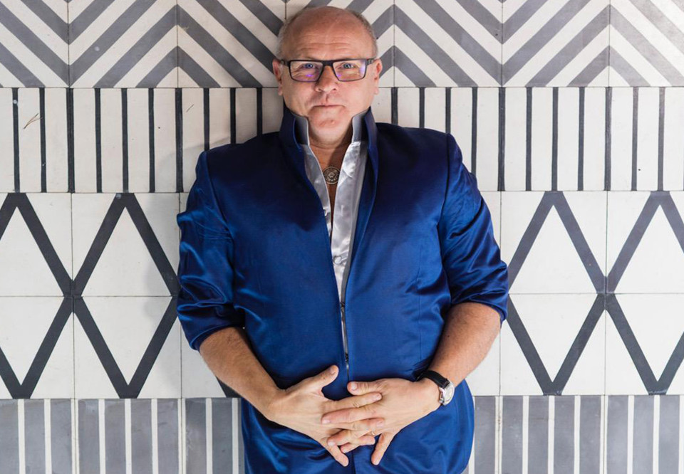 Man som står mot en mönstrad vägg. Fotografi.