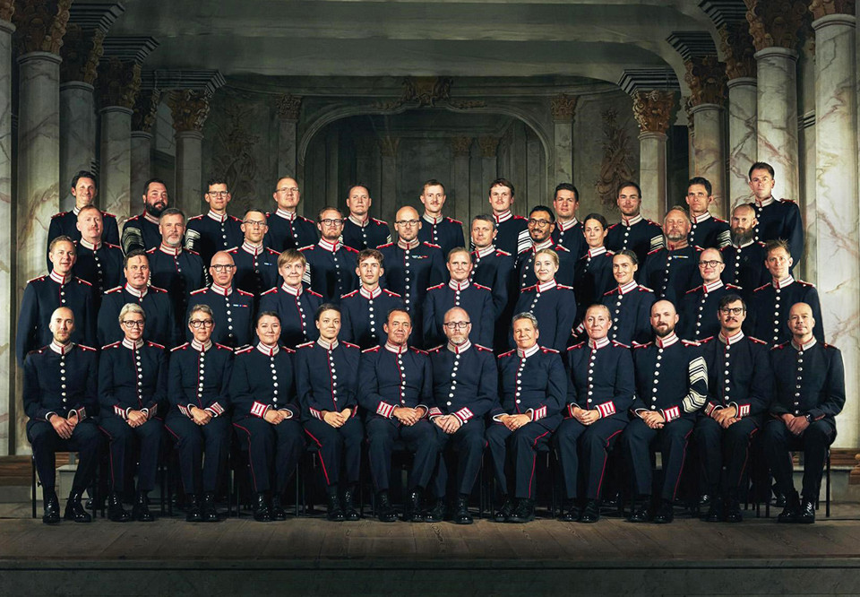Musicians in uniform, lined up in four rows behind each other. Photograph.