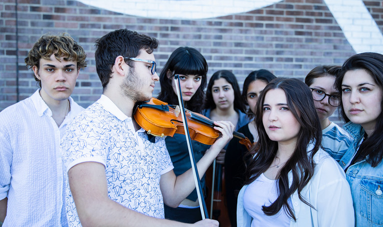 A group of young people, one is playing the violin. Photograph.