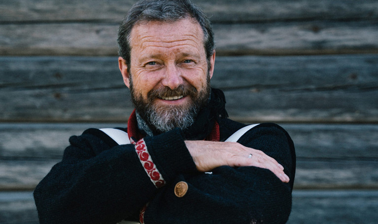 A man with a cap sitting down, casually leaning over the backrest of a chair. Photograph.